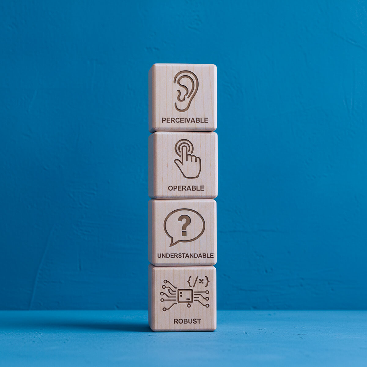 Quattro cubi di legno impilati, ciascuno con un’icona per i principi POUR dell’accessibilità : Percepibile, Operabile, Comprensibile, Robusto